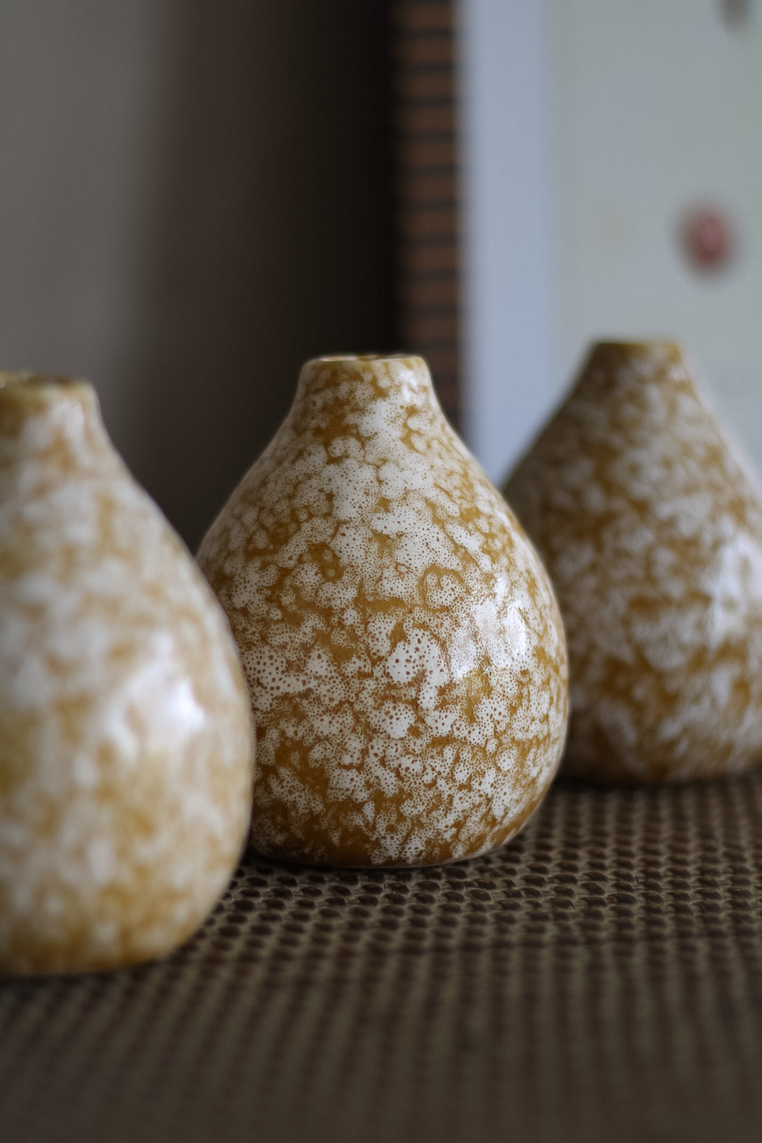 Three ceramic bud vases with a speckled pattern on a textured surface.