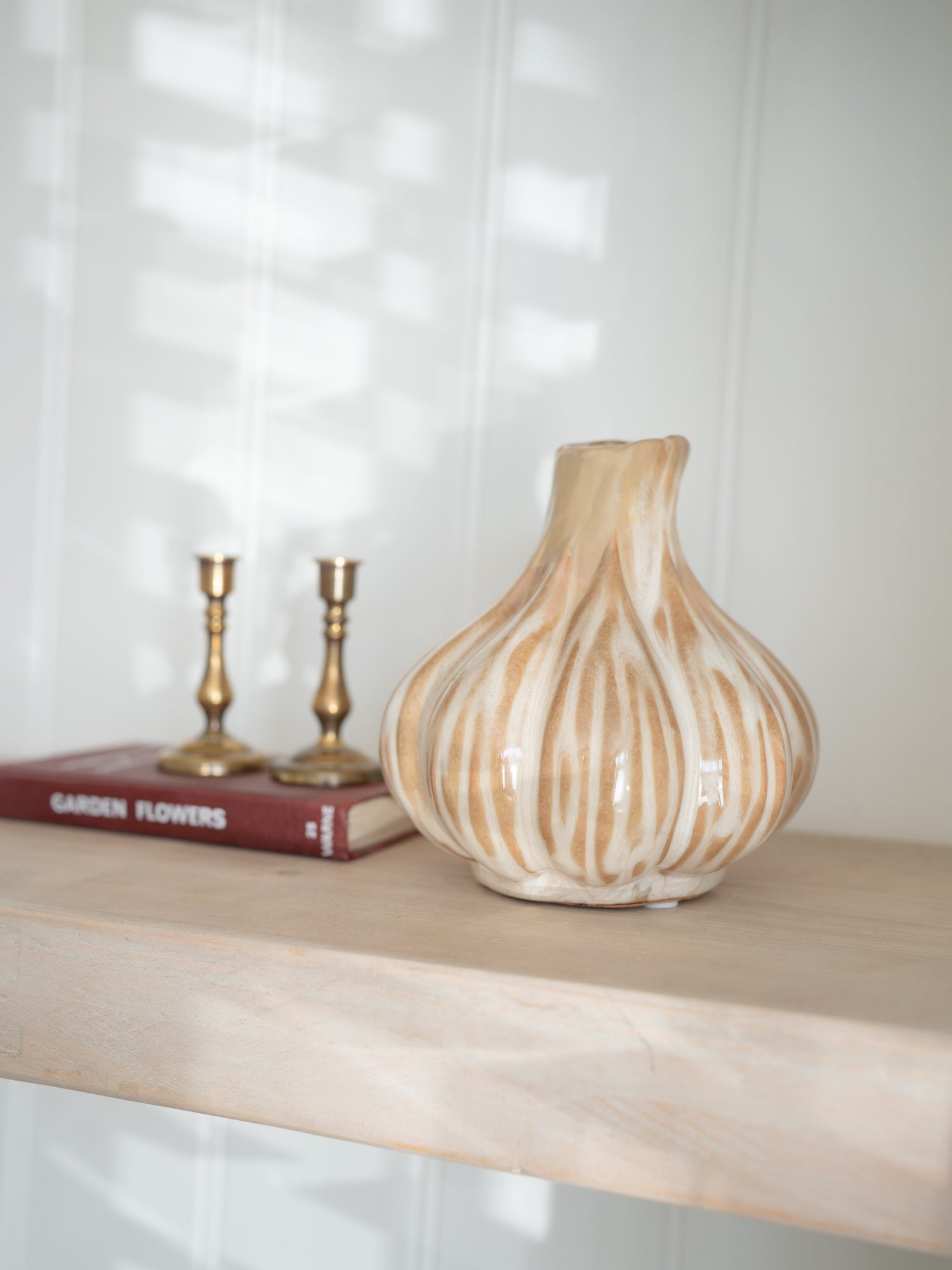 Decorative ceramic beige onion vase on a wooden shelf with books and candle holders in the background.