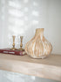Decorative ceramic beige onion vase on a wooden shelf with books and candle holders in the background.