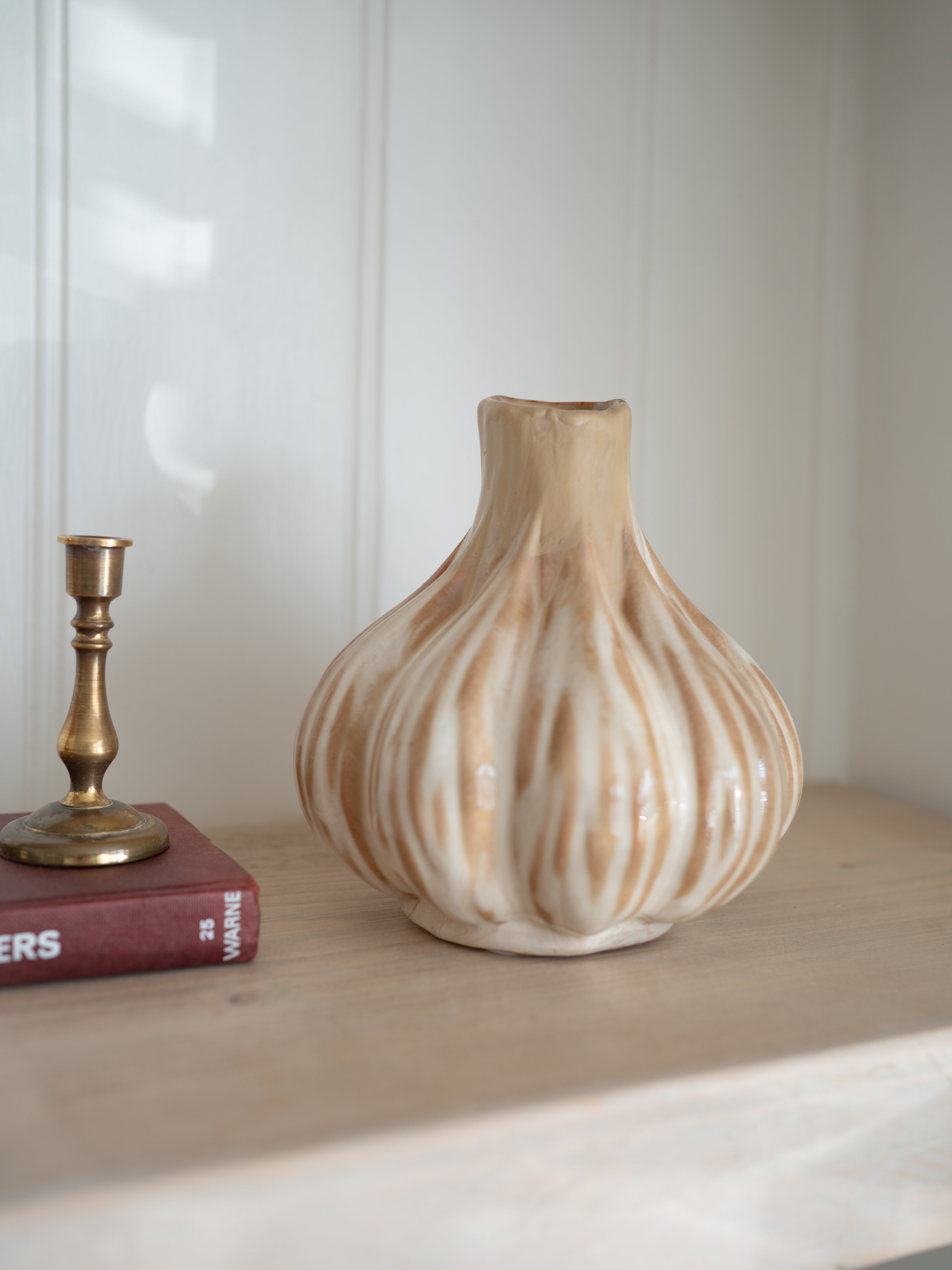 Decorative ceramic onion beige vase on a shelf with a book and candlestick in the background