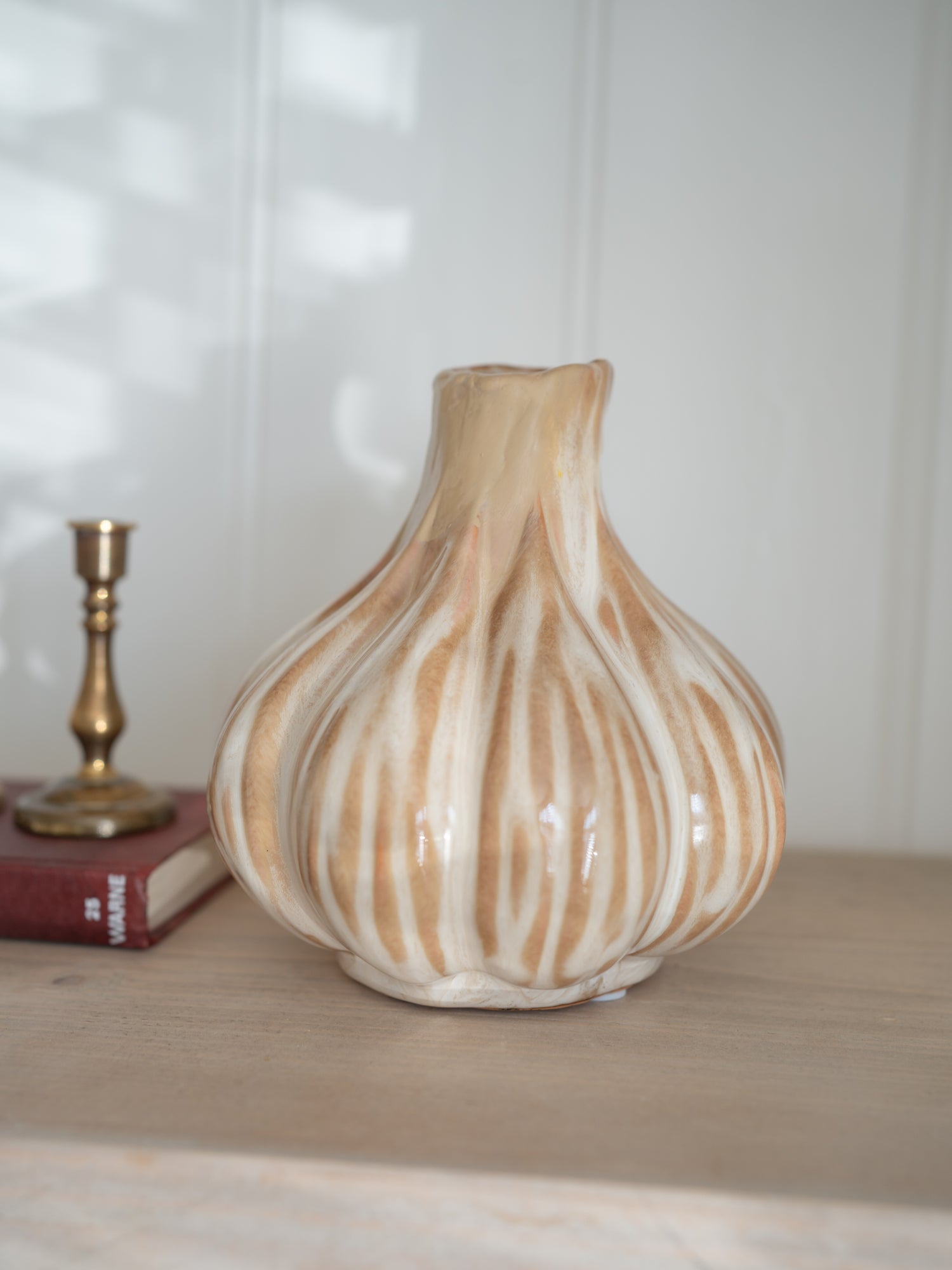Decorative ceramic beige onion shaped vase with brown and white stripes on a wooden surface.
