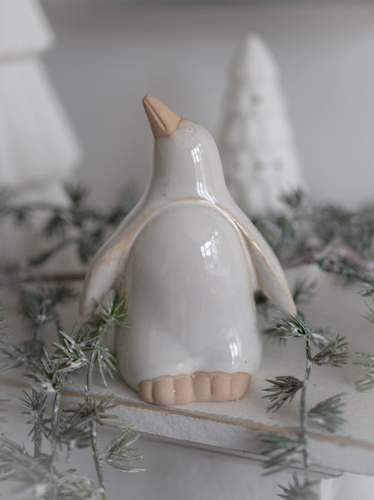 White ceramic penguin figurine on a decorative surface with greenery