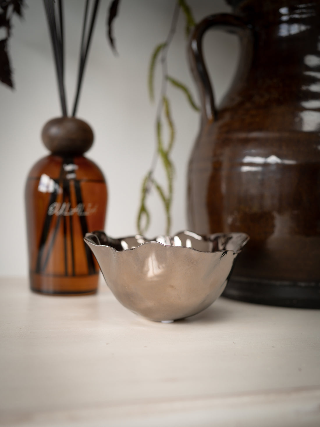 Copper bowl on a surface with a blurred background featuring a bottle and a vase.