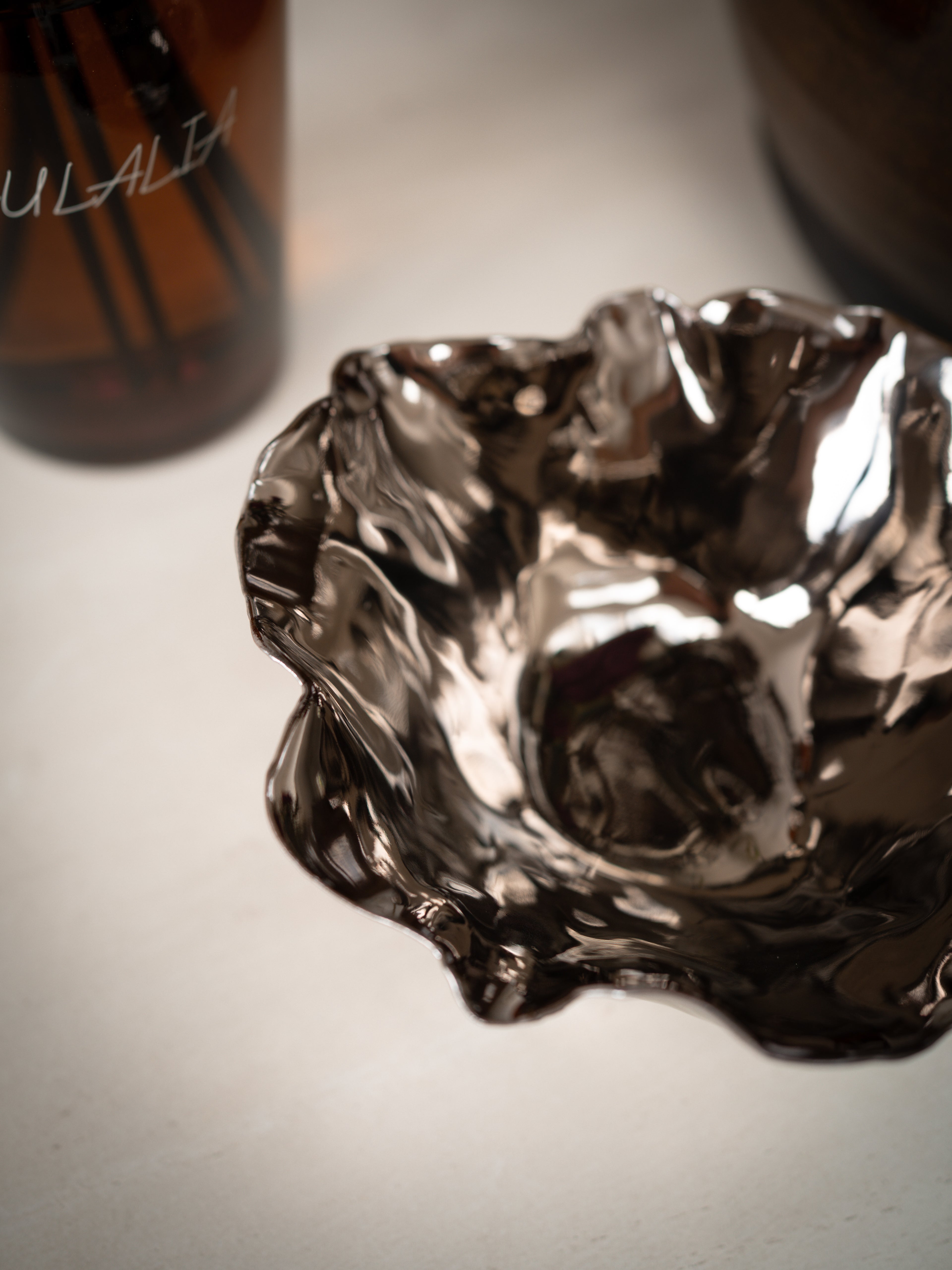 Metallic bowl on a light surface with a blurred bottle in the background