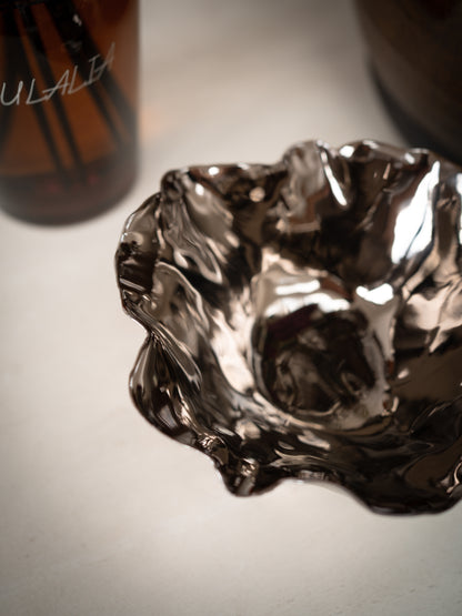 Metallic bowl on a light surface with a blurred bottle in the background