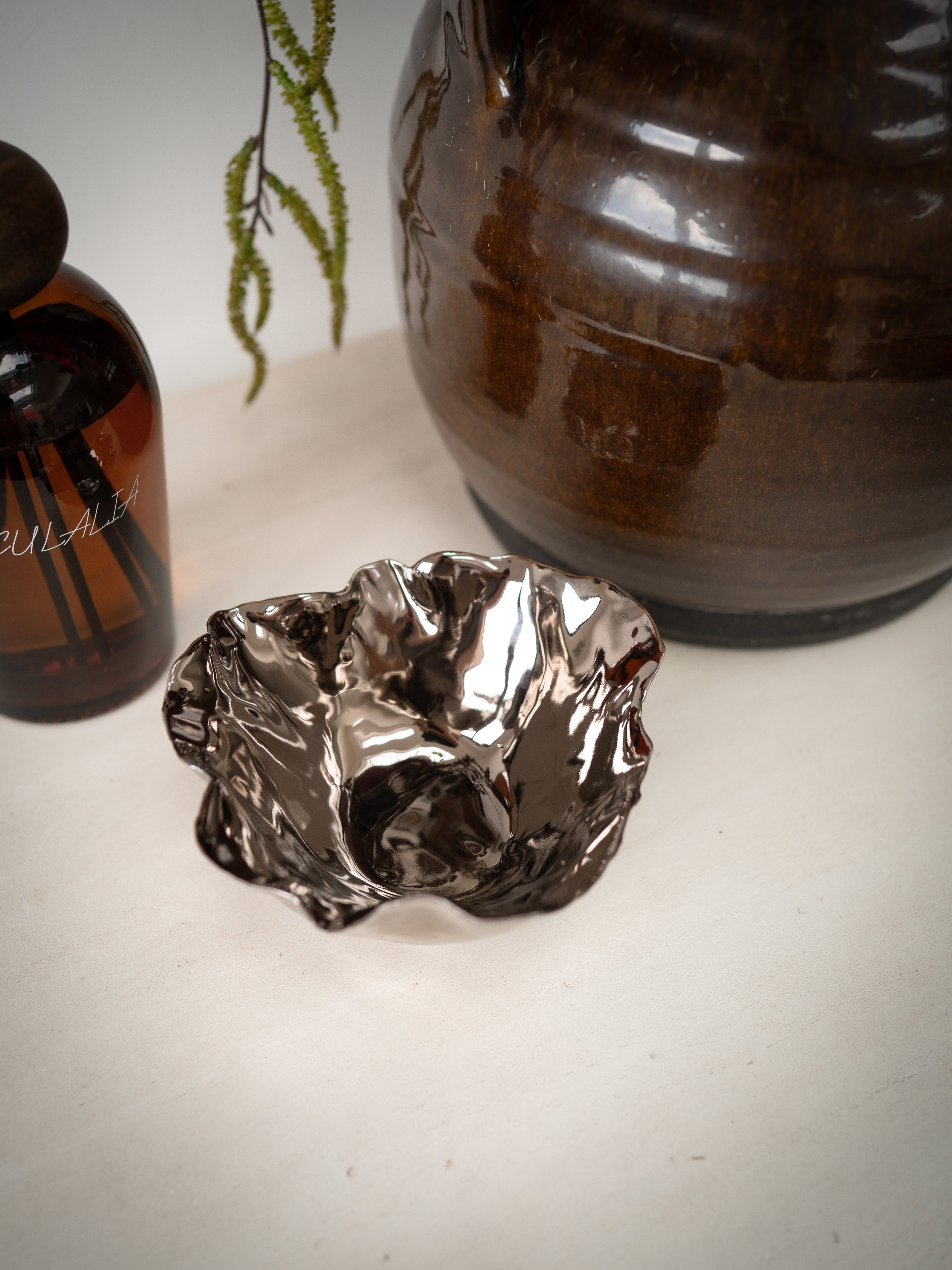 Metallic copper decorative ceramic bowl on a white surface with a bottle and vase in the background