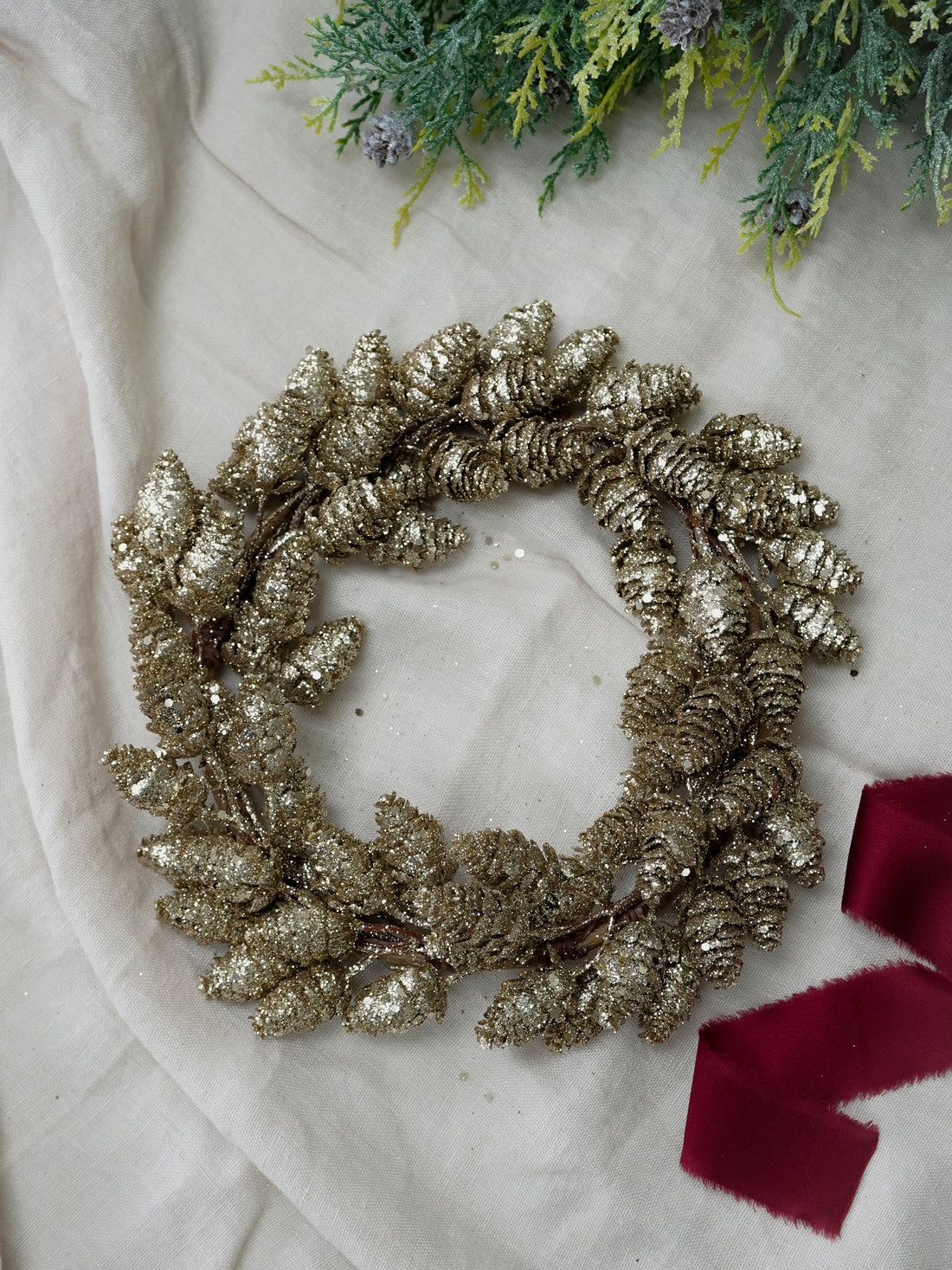 Gold glittery wreath on a light background with a red ribbon