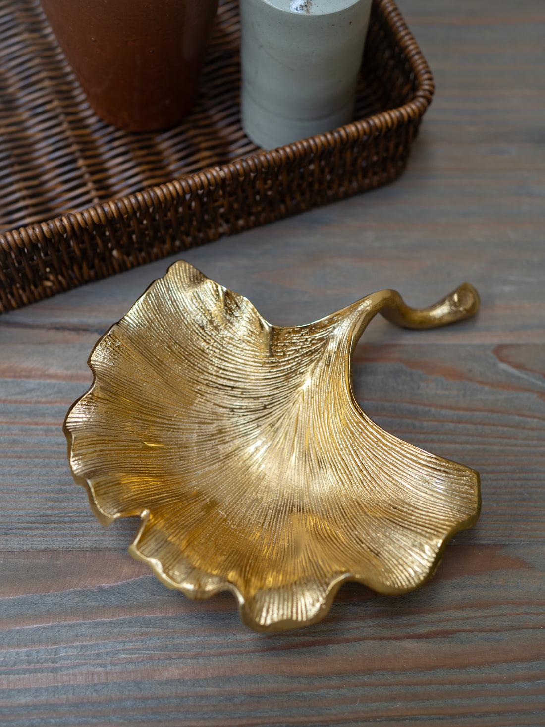 Gold leaf-shaped decorative trinket dish on a wooden surface with a wicker basket in the background.