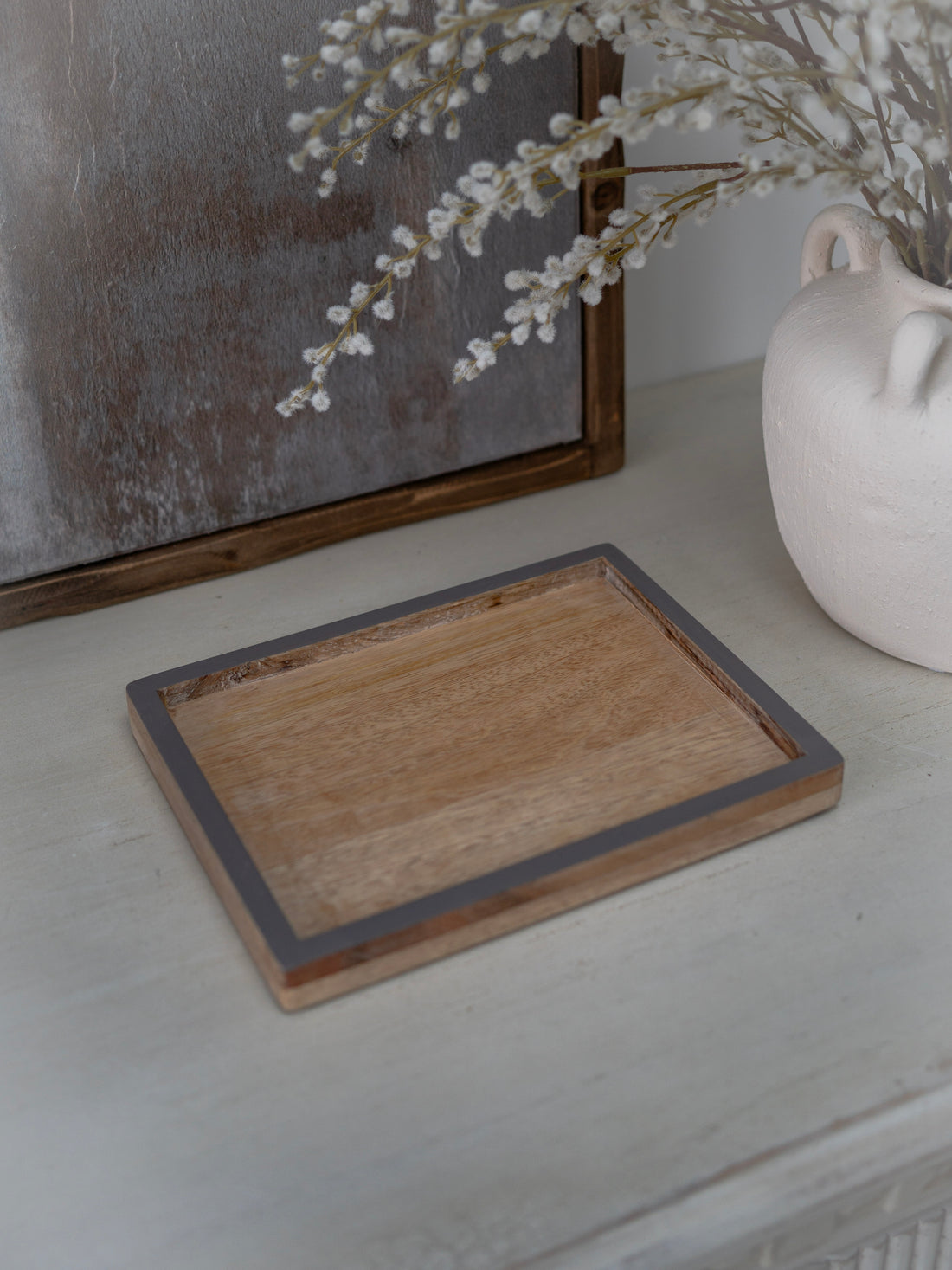 Wooden tray on a white surface with a vase and decorative elements in the background