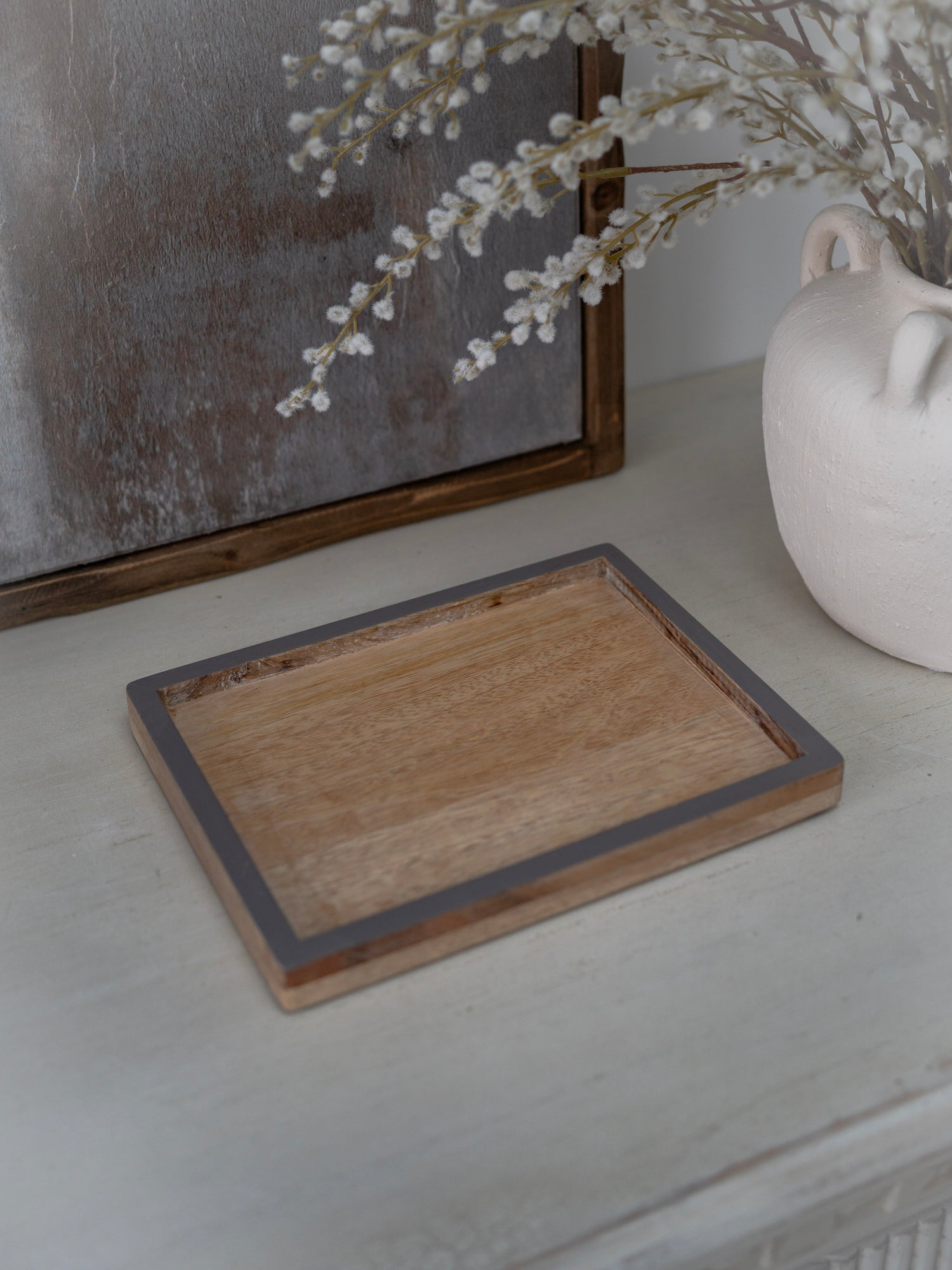 Wooden tray on a white surface with a vase and decorative elements in the background