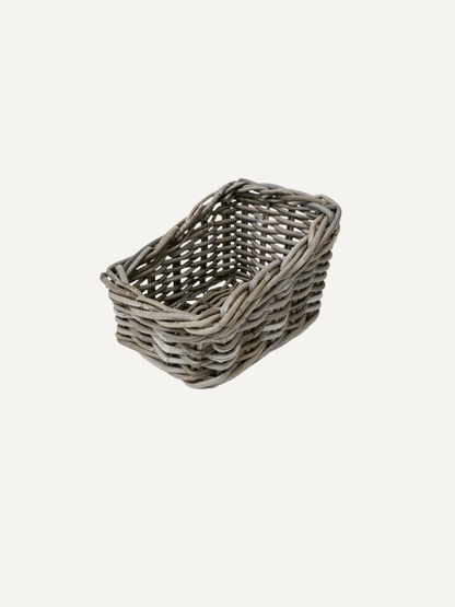 A small rectangular woven basket made from gray wicker or rattan, shown on a plain light gray background.