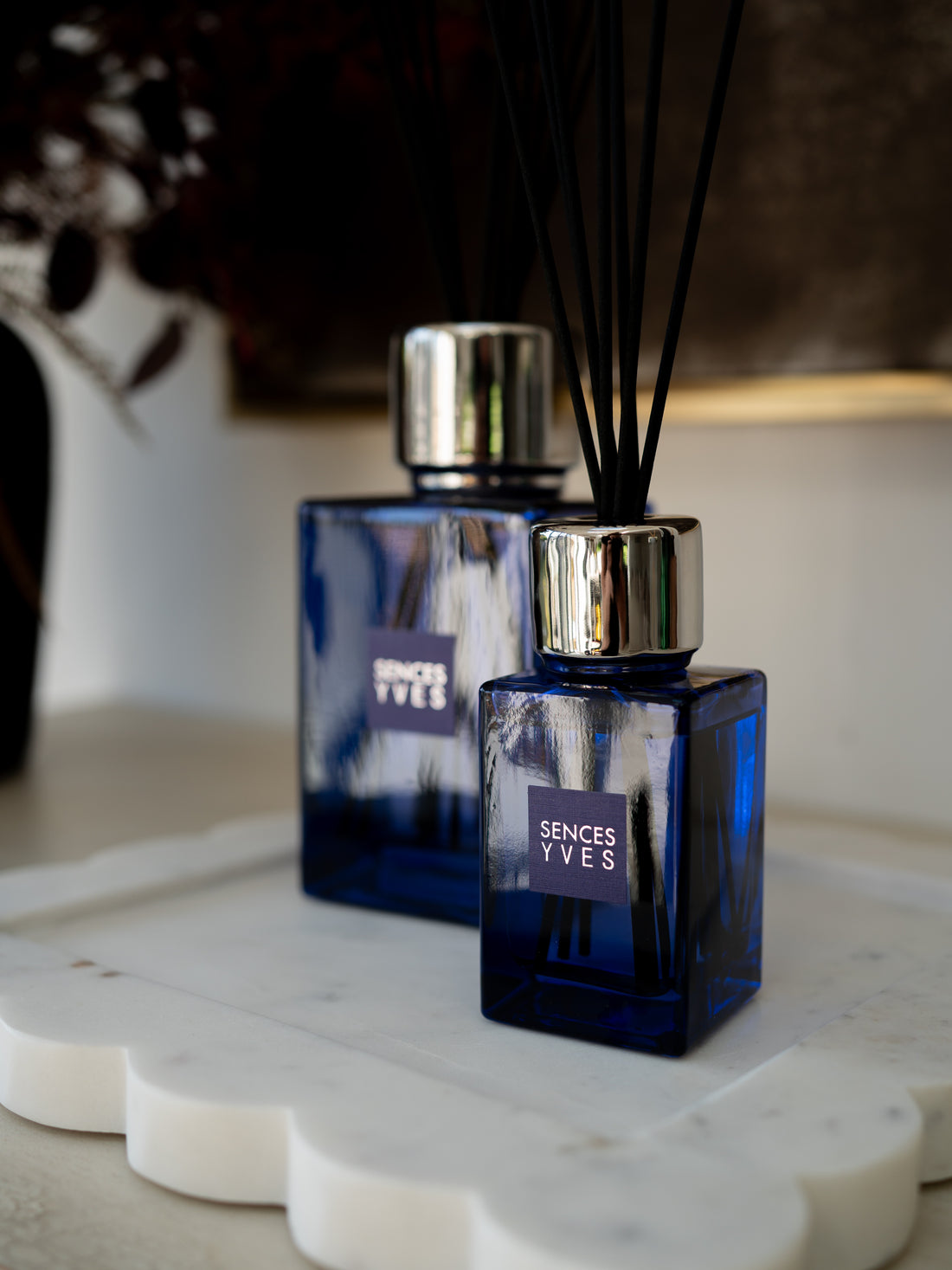 Two blue glass reed diffusers with silver caps and black reeds, labeled &