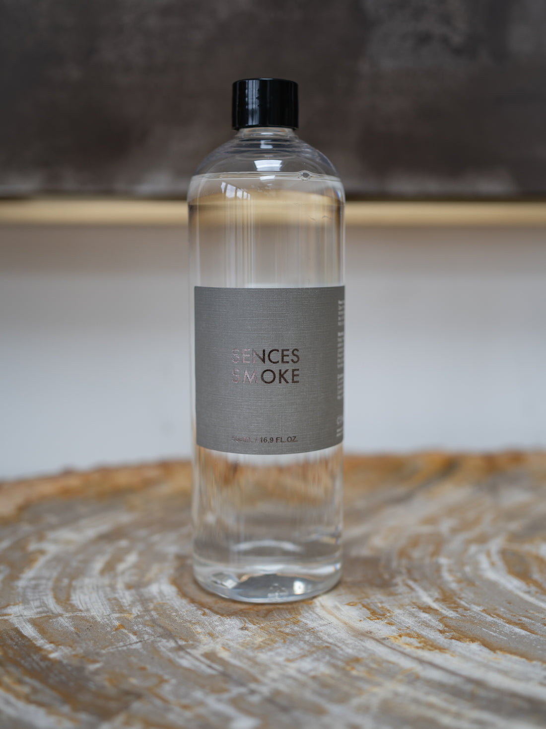 A clear plastic bottle of Scented Senses Smoke fragrance oil with a black cap and a gray label, sitting on a rustic wood slice coaster.