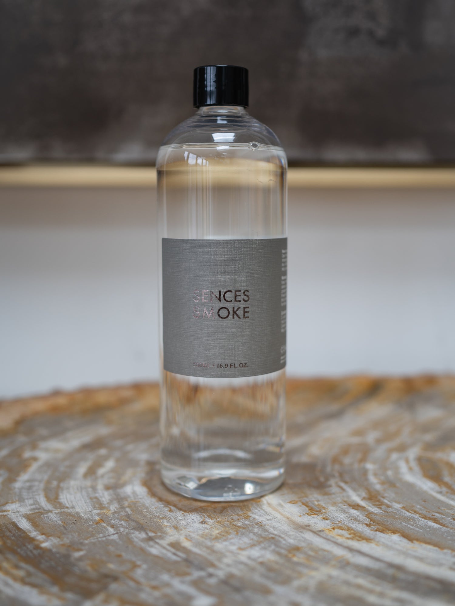 A clear plastic bottle of Scented Senses Smoke fragrance oil with a black cap and a gray label, sitting on a rustic wood slice coaster.