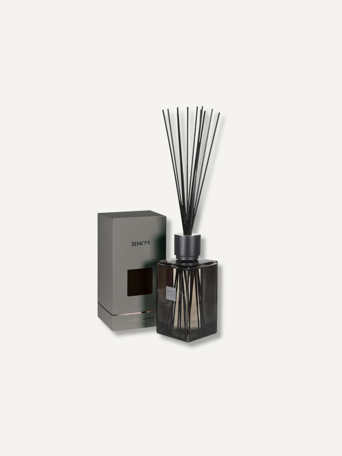 A reed diffuser bottle with dark glass and black reeds, shown next to its gray rectangular box on a plain light background.
