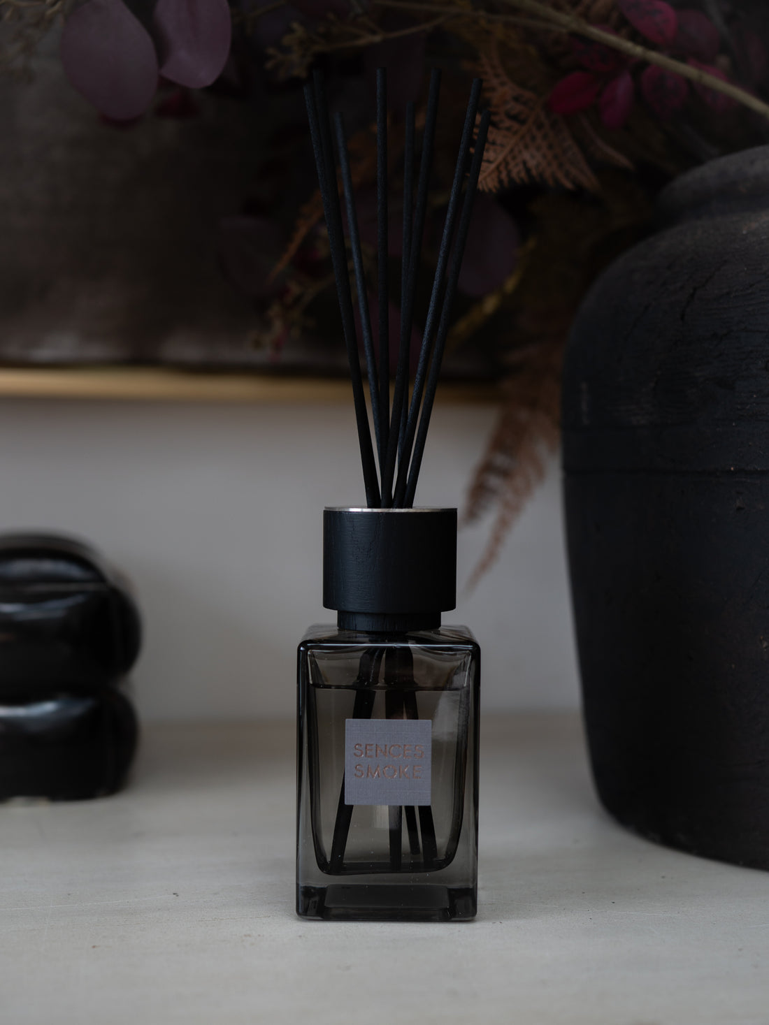 A dark glass reed diffuser bottle with a matte black cap and black reeds, labeled &