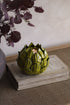 Artichoke-shaped candle holder on a wooden surface with a blurred background