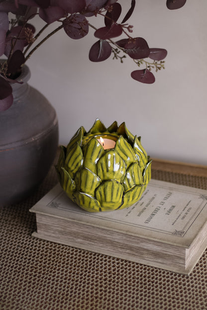 Green ceramic artichoke-shaped candle on a book with a blurred background
