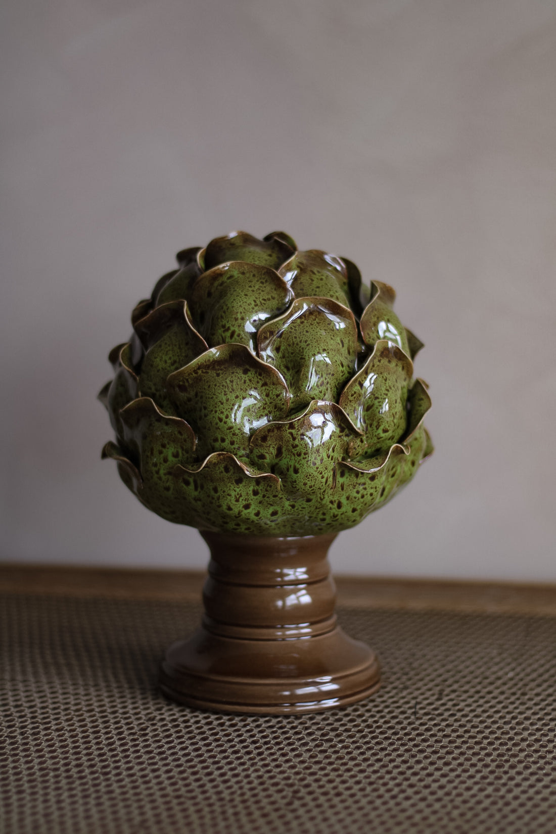 Green ceramic artichoke on a brown stand against a plain background