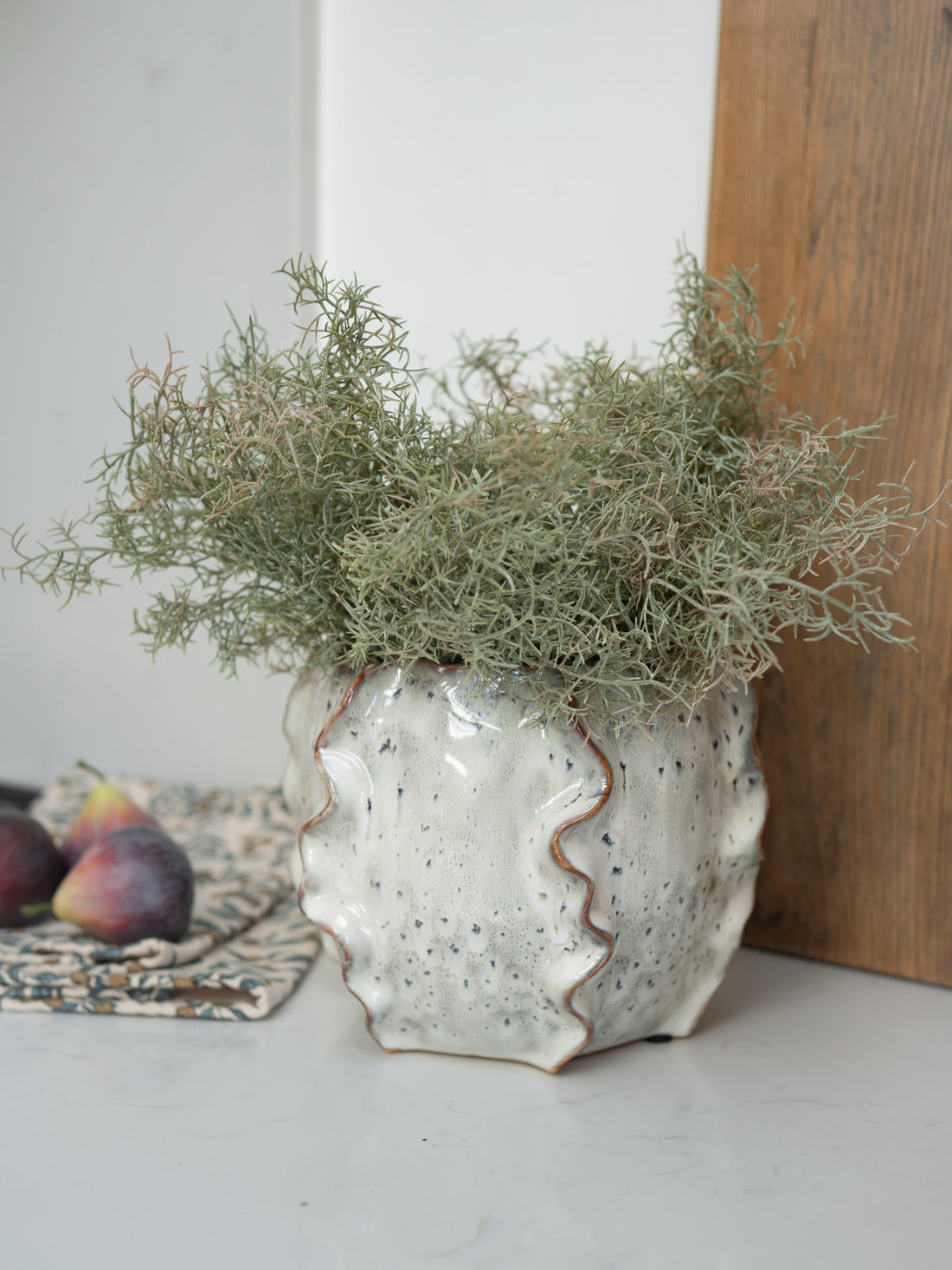 Soft Beige Ceramic Wave Vase with faux spanish moss bush and faux figs in the background on white marble surface