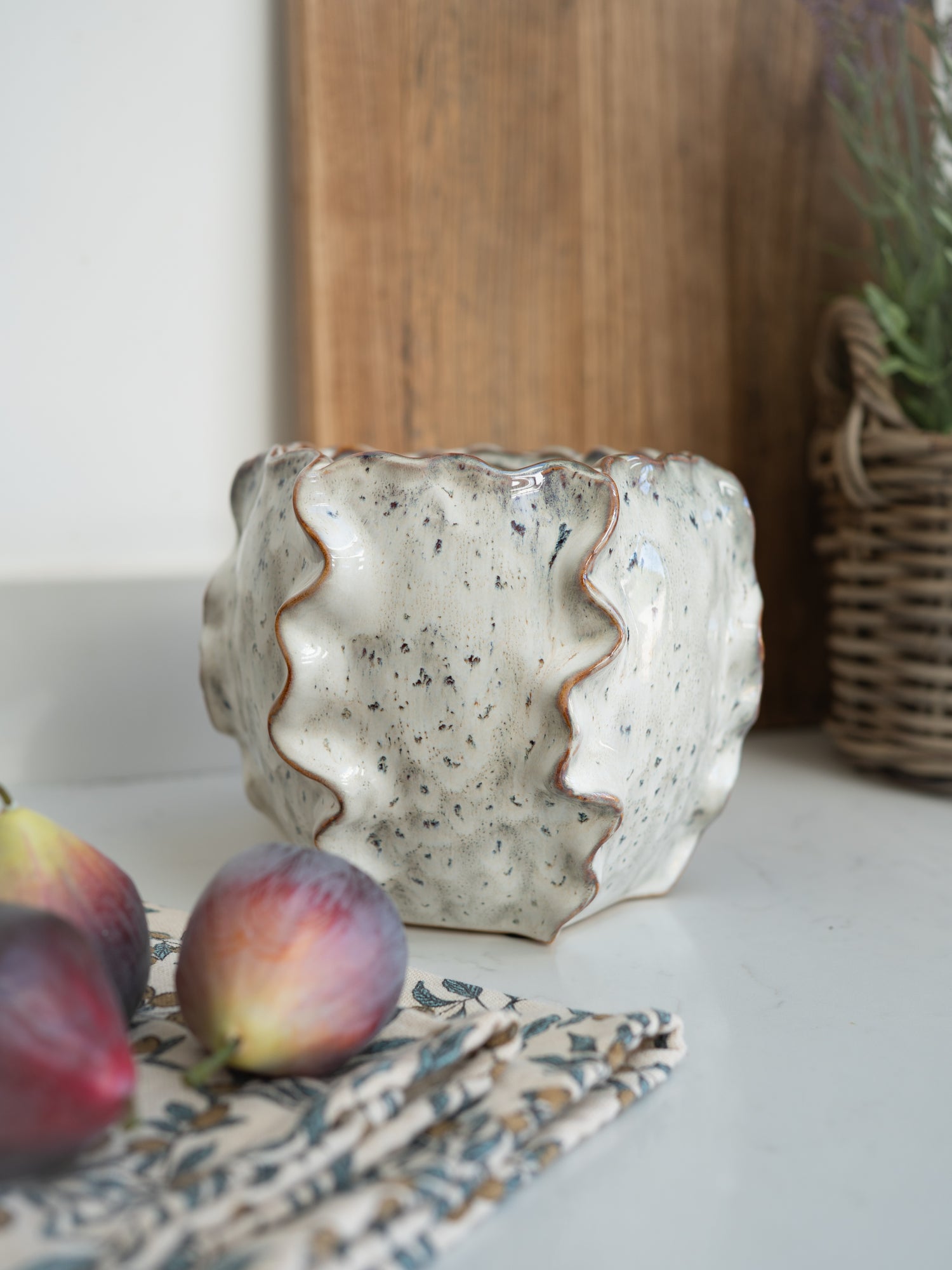 Ceramic pot with wavy design on a surface with fruits and a plant in the background