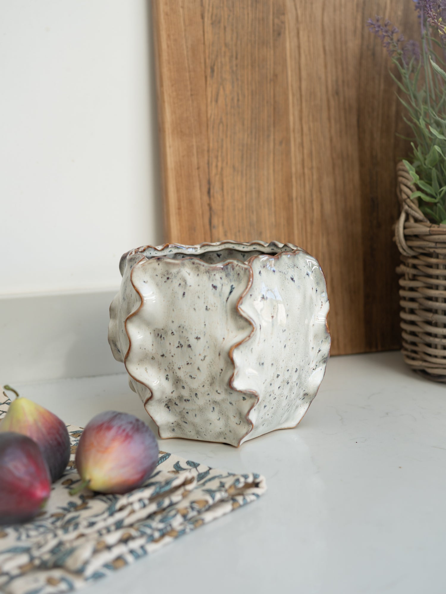 Decorative ceramic vase on a surface with figs and a wooden board in the background