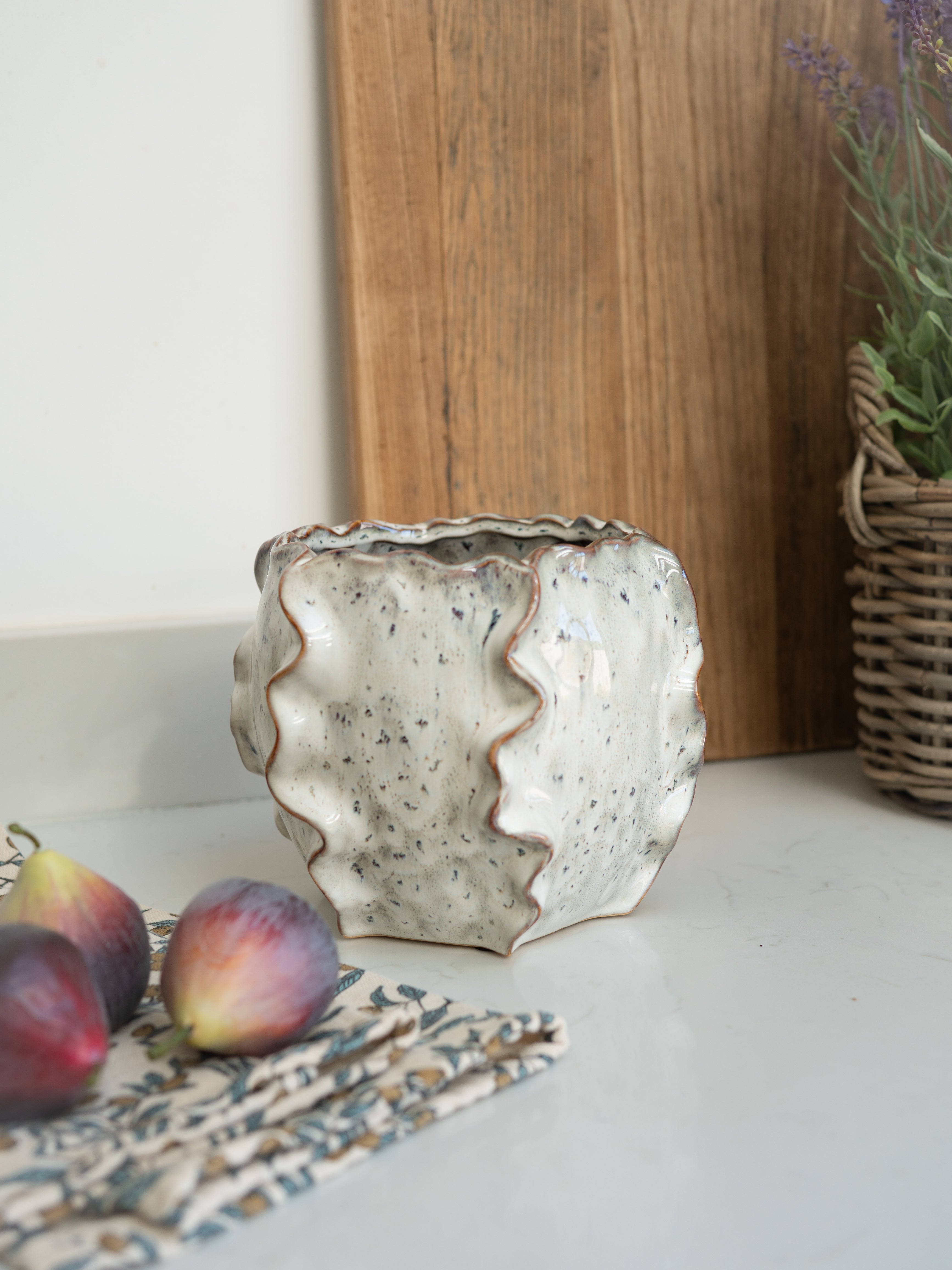 Decorative ceramic vase on a surface with figs and a wooden board in the background