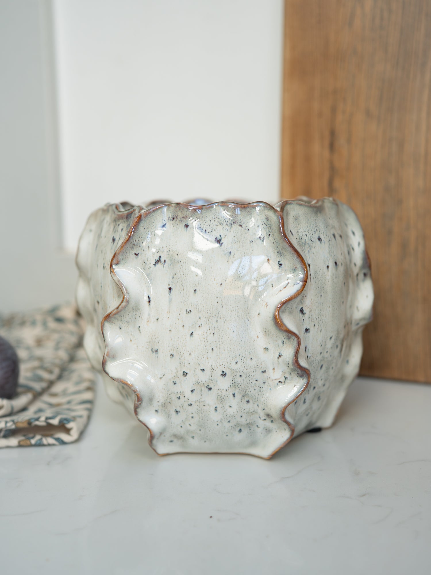Speckled ceramic vase on a white surface with a wooden board in the background