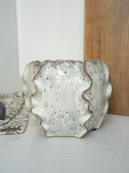 Speckled ceramic vase on a white surface with a wooden board in the background
