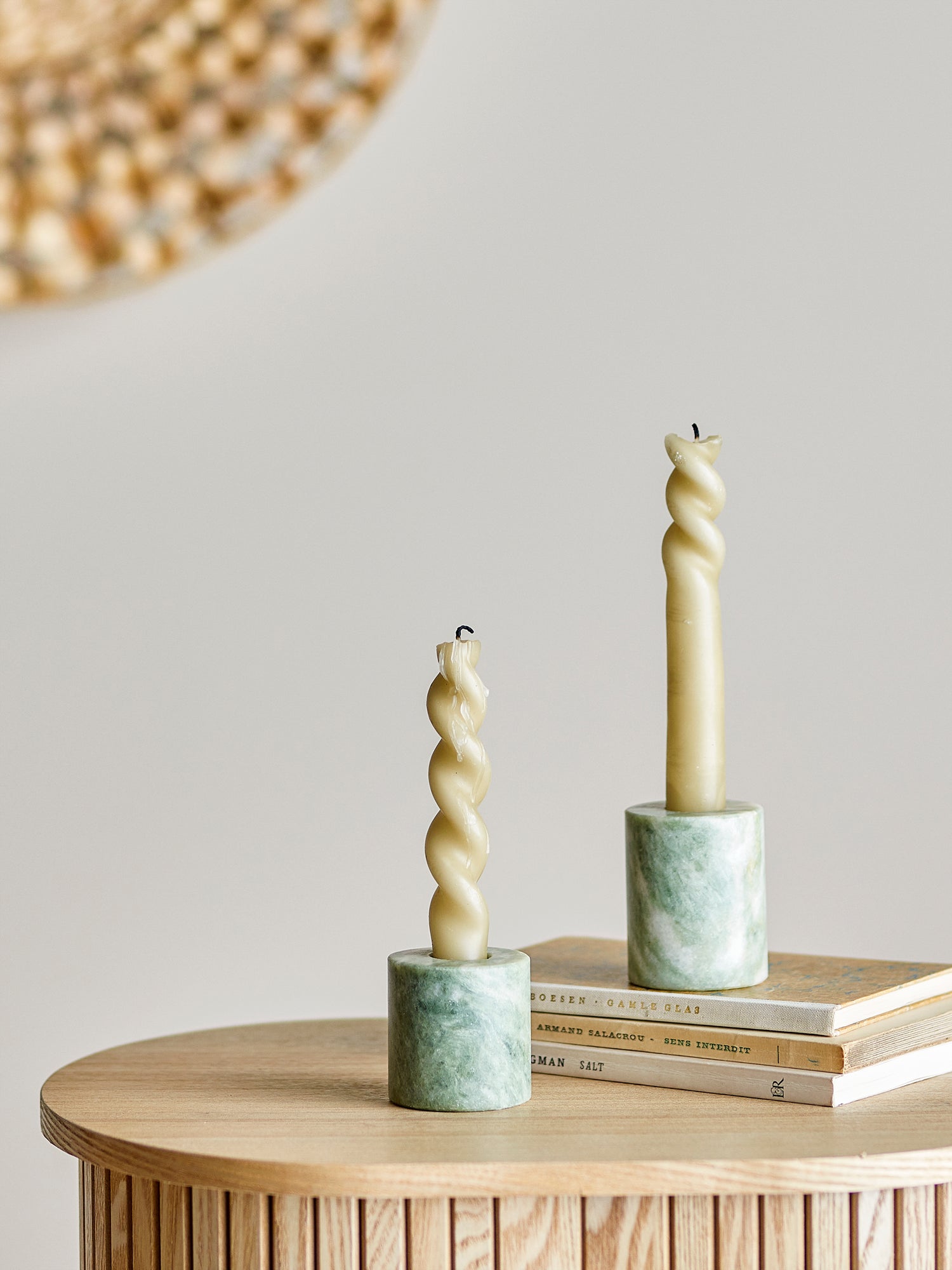 Two twisted candles in marble holders on a wooden surface with a neutral background