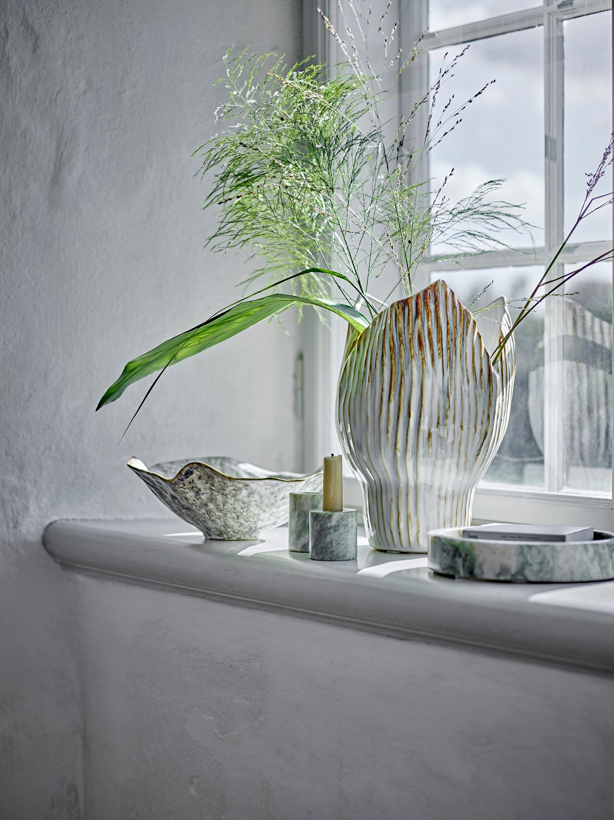 Decorative setting with a vase, candle, and bowls on a windowsill.