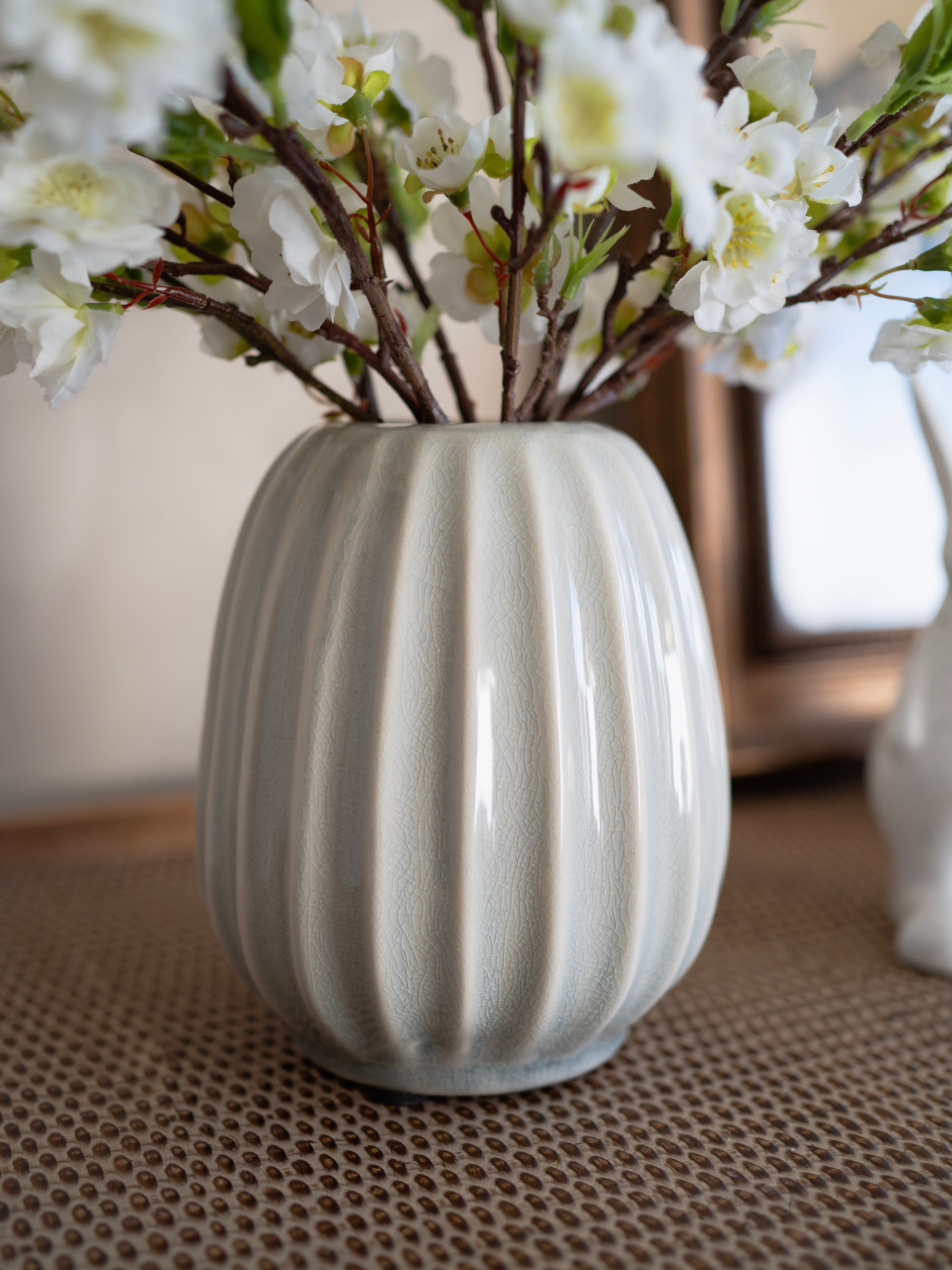 Grey ribbed vase with white flowers on a textured surface