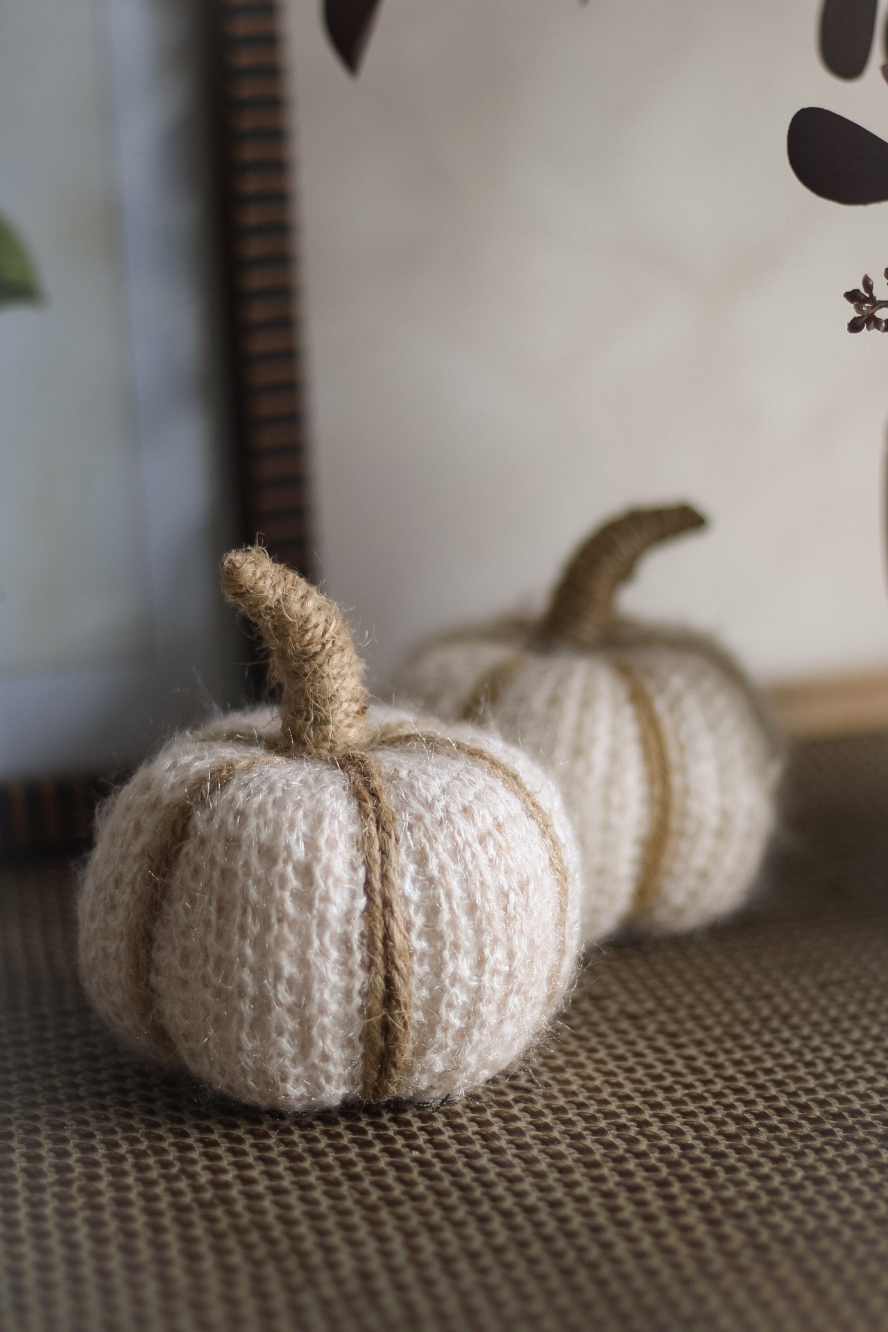 Two soft white and taupe pumpkins on a textured surface with a neutral background