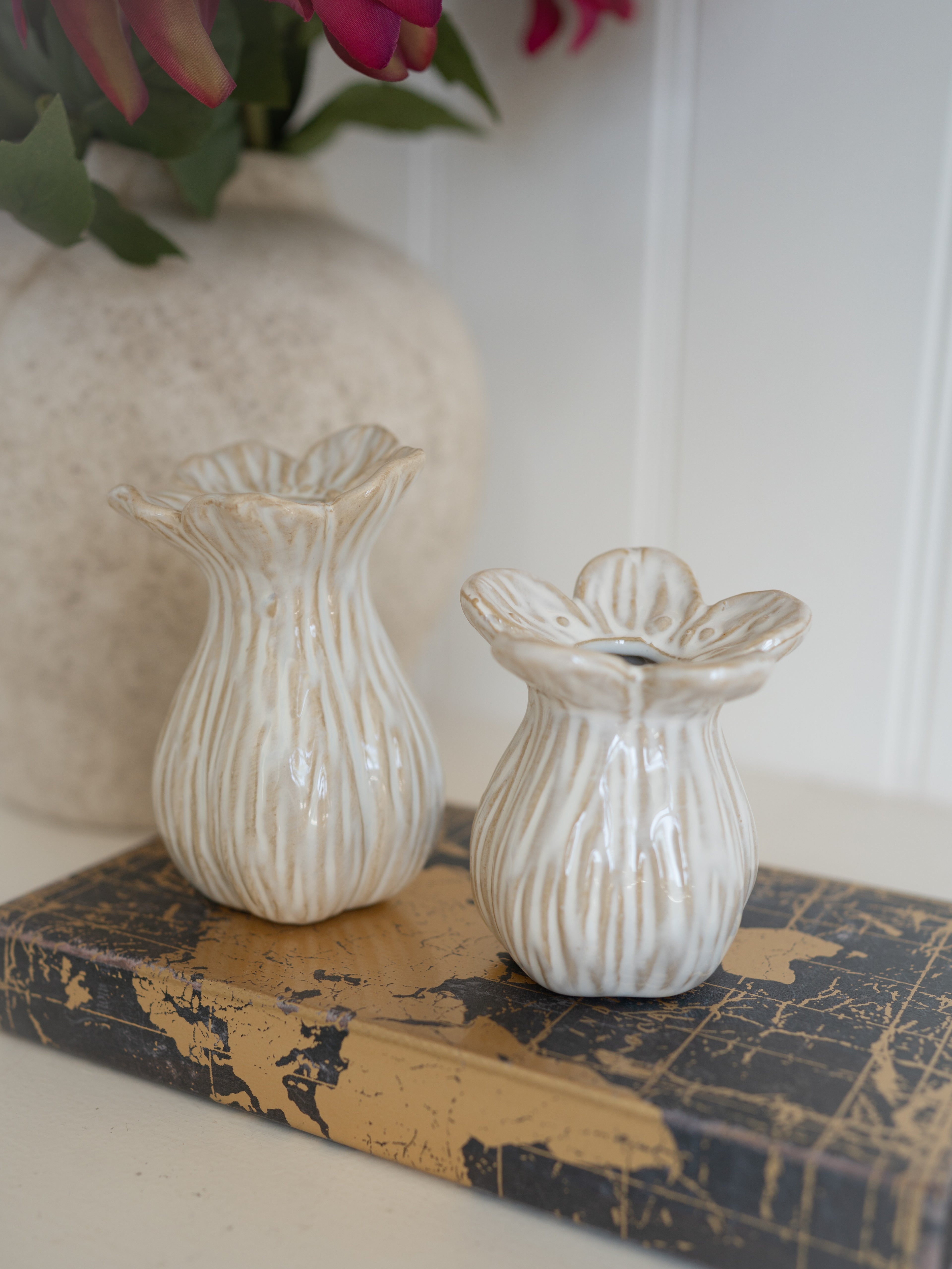 Two decorative ceramic bud vases on a textured surface with a blurred background