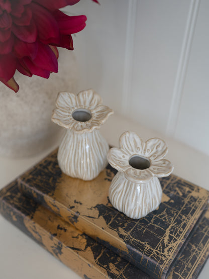 Two ceramic flower-shaped candle holders on an old book with a red flower in the background.