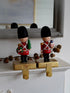 Two toy soldiers in red uniforms with black hats on a decorative stand.