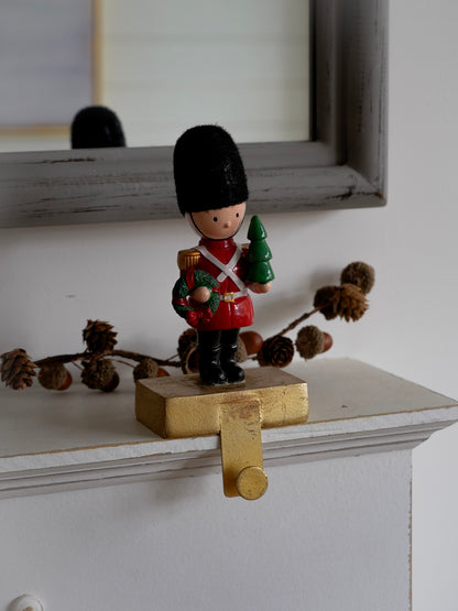 Small figurine of a guard holding a Christmas tree on a decorative shelf.