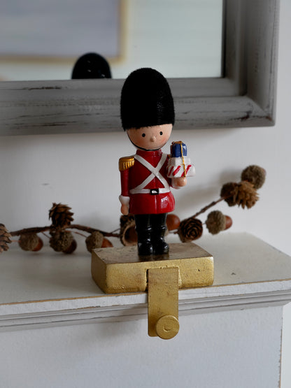 Small figurine of a guard in red uniform with a toy炮 on a wooden surface.