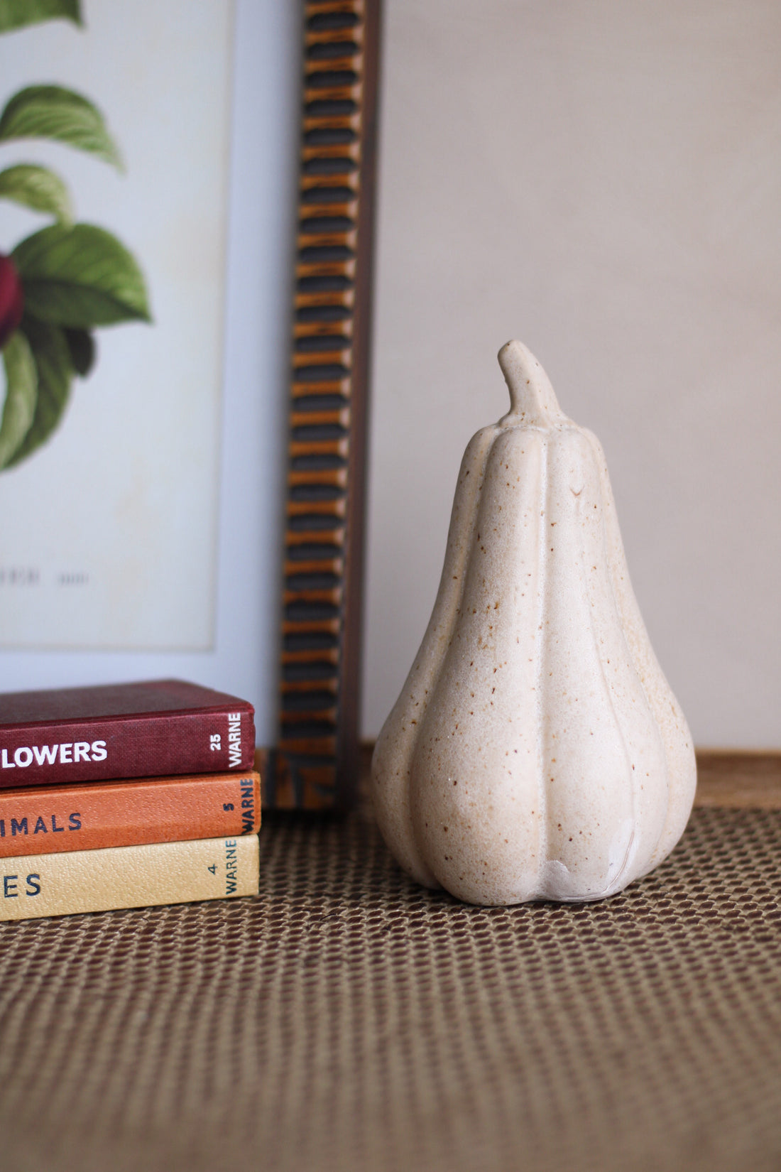 Decorative white gourd pumpkin object on a textured surface with books and a framed picture in the background.