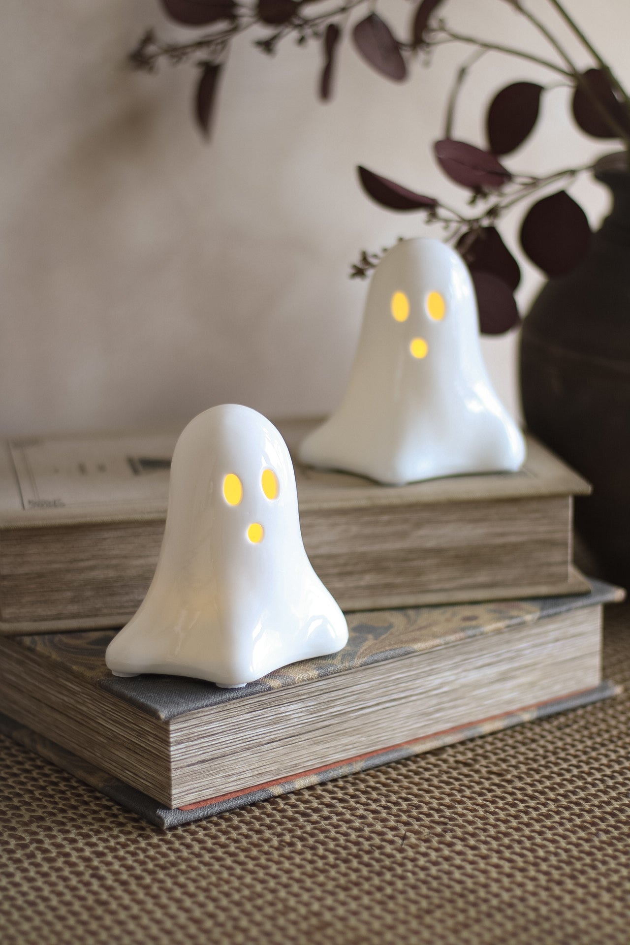 Two ghost-shaped LED decorations with glowing yellow eyes on top of books.