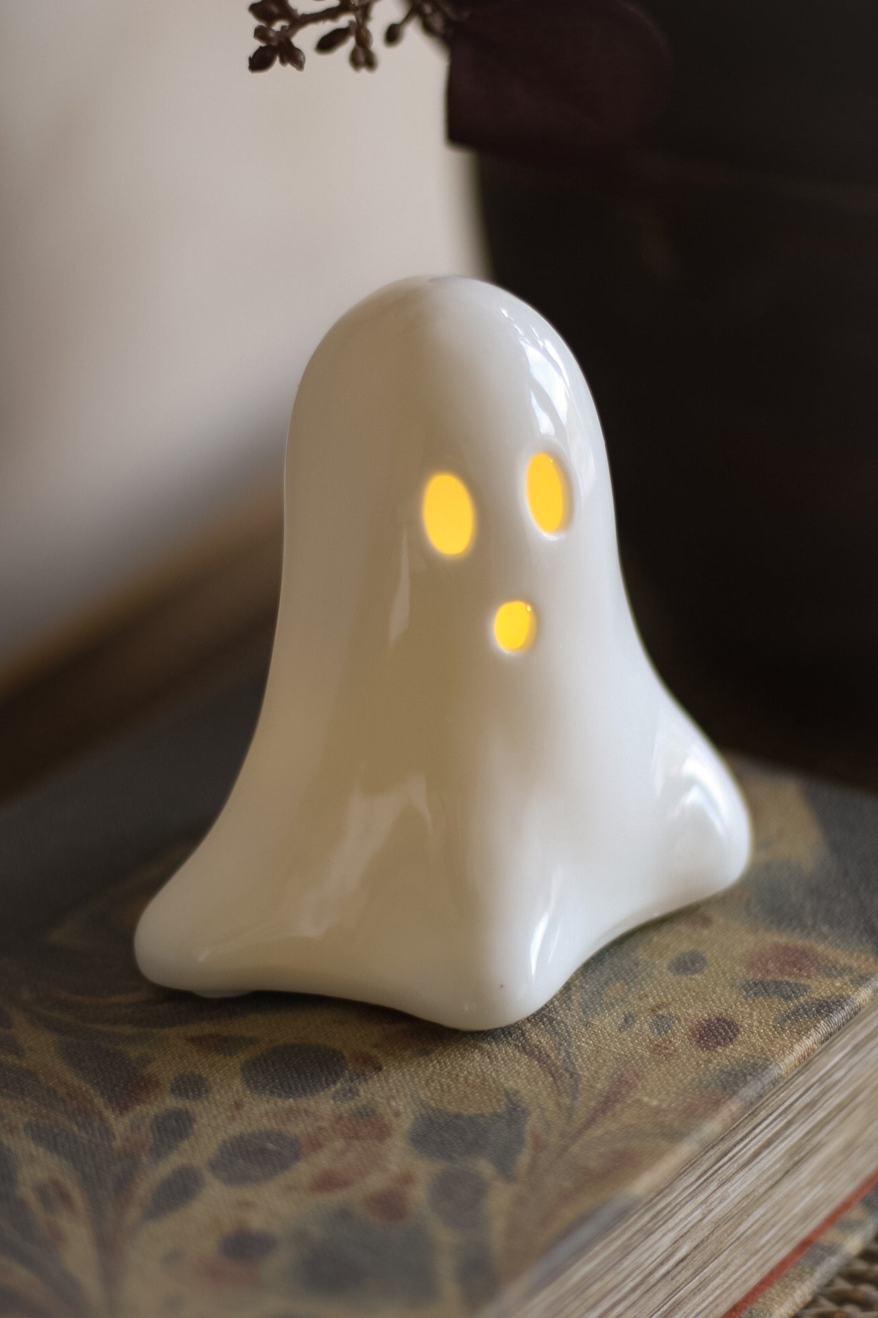 White ghost-shaped ceramic LED decoration with glowing eyes on a patterned surface