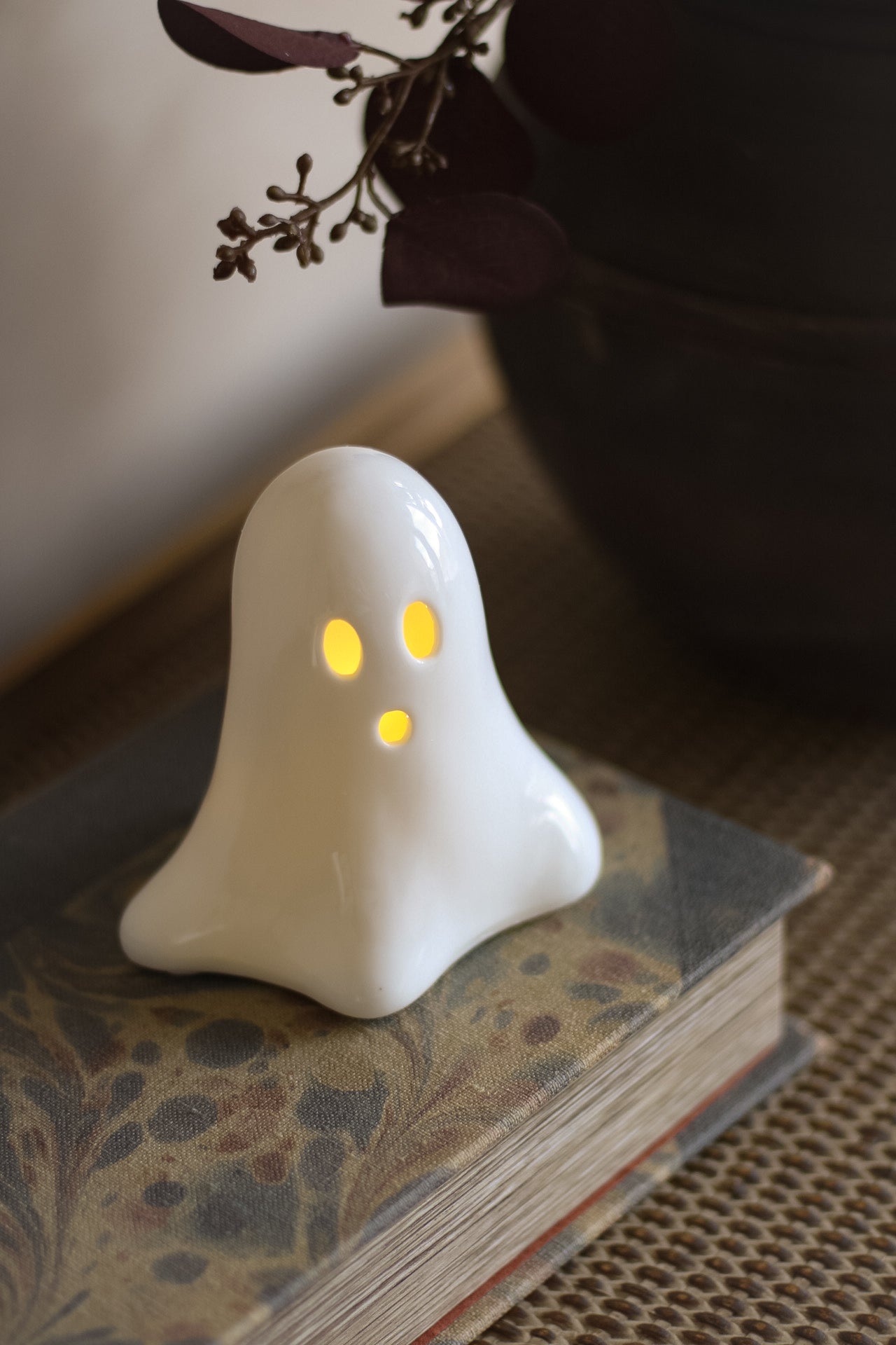 White ghost-shaped ceramic LED decoration with glowing eyes on a book