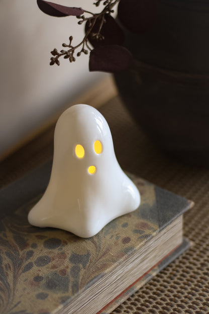 White ghost-shaped ceramic LED decoration with glowing eyes on a book