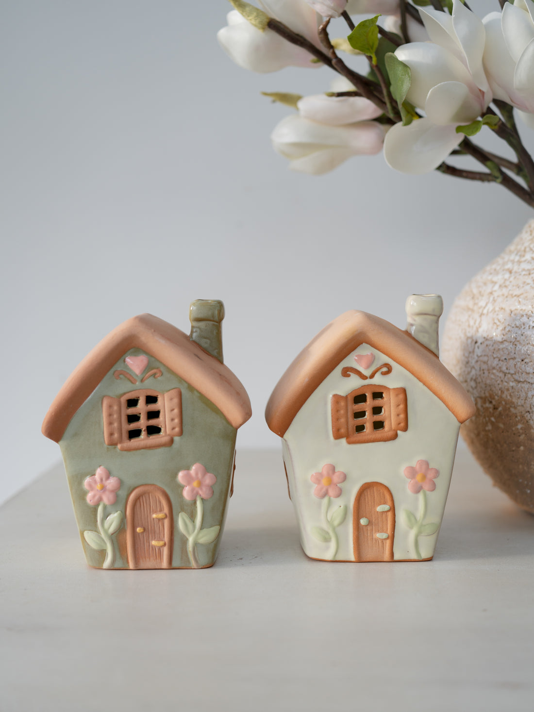 Two ceramic house-shaped planters with decorative elements on a light gray background.