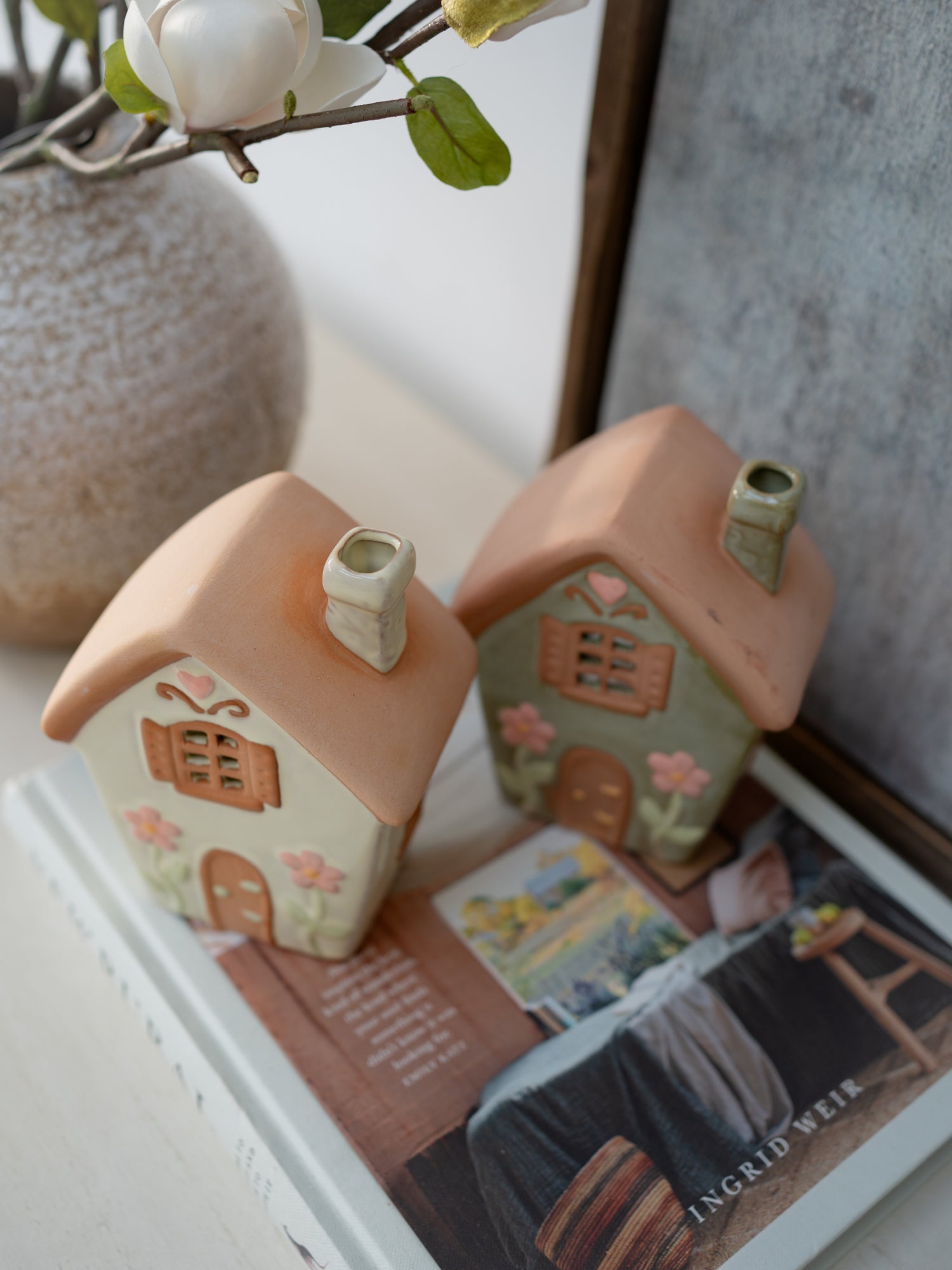 Two small ceramic house-shaped vases on a book with a blurred background