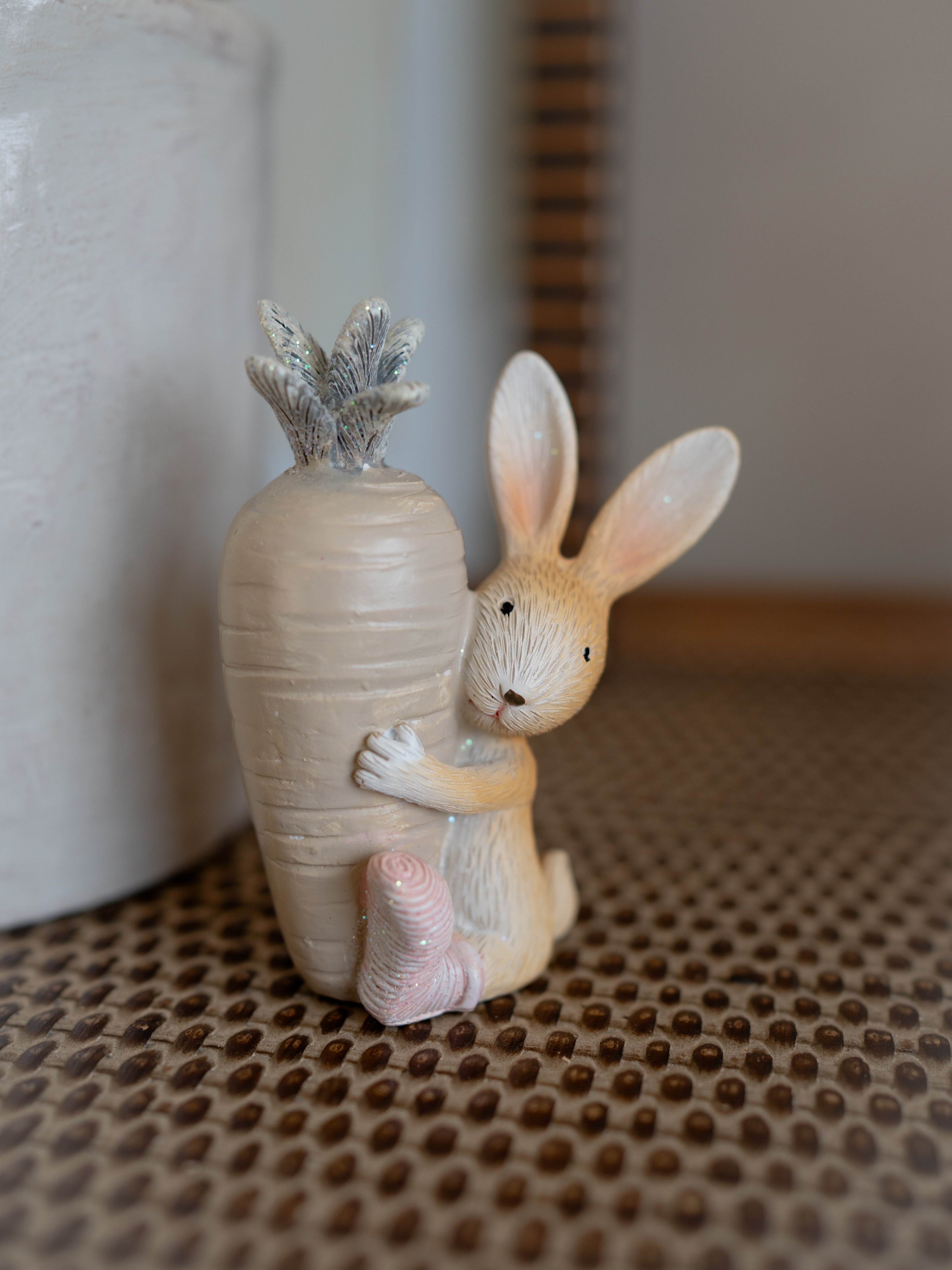 Decorative figurine of a rabbit holding a carrot-shaped vase on a textured surface.