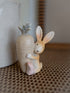 Decorative figurine of a rabbit holding a carrot-shaped vase on a textured surface.