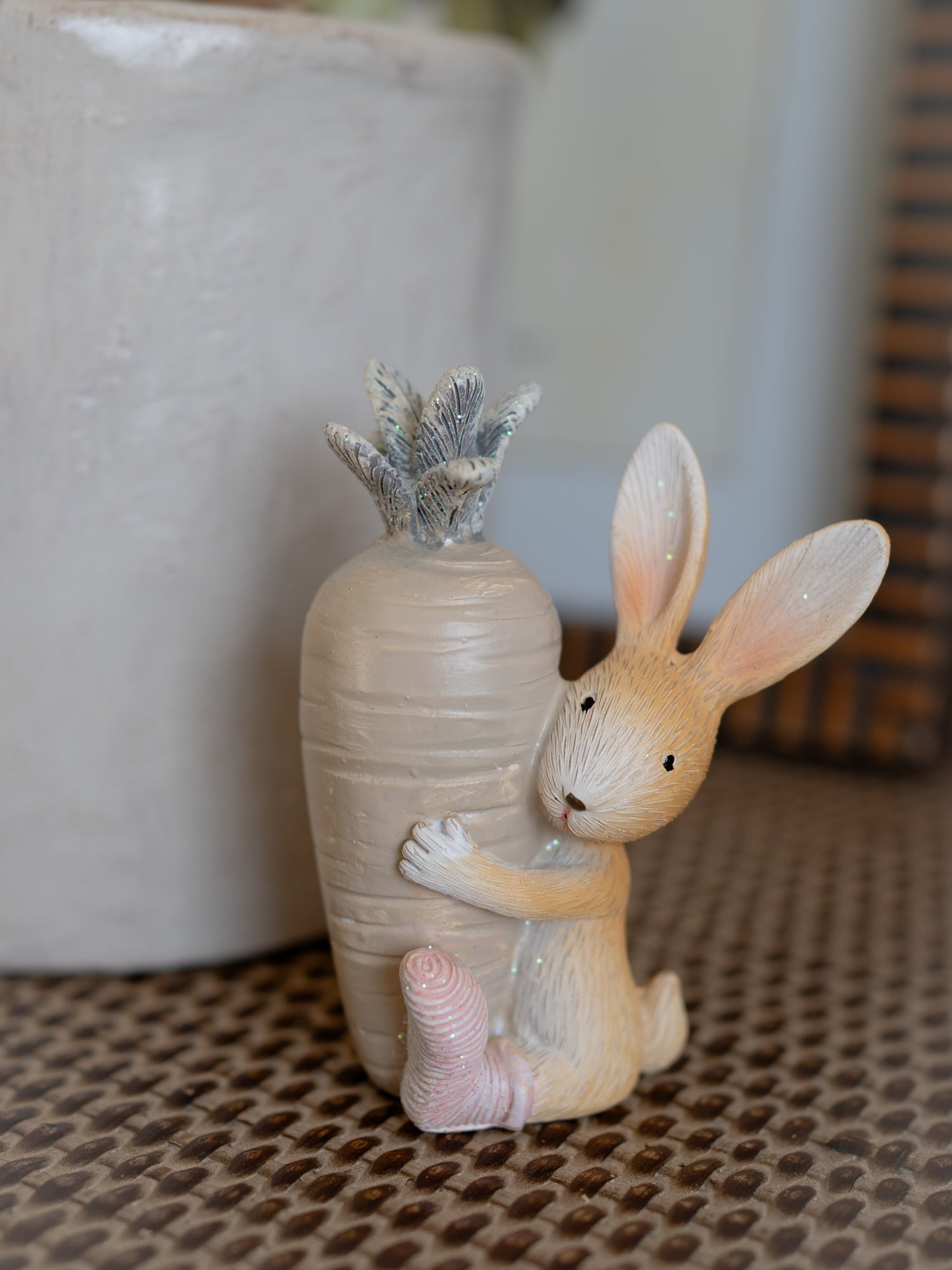 Decorative figurine of a rabbit embracing a textured vase with a plant on a patterned surface.