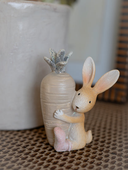 Decorative figurine of a rabbit embracing a textured vase with a plant on a patterned surface.