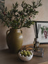 Decorative setting with a vase of greenery, a bowl of green balls, and a diffuser on a table.
